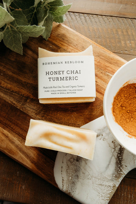 Bar of honey chai turmeric soap with 'Bohemian Rebloom' label on a wooden board with a cup of tea and leaves.