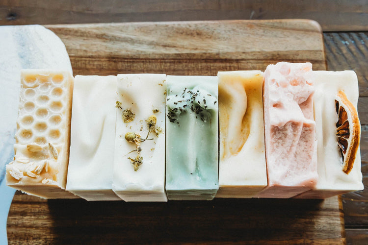 Several different bars of soap of different colors located on a cutting board.