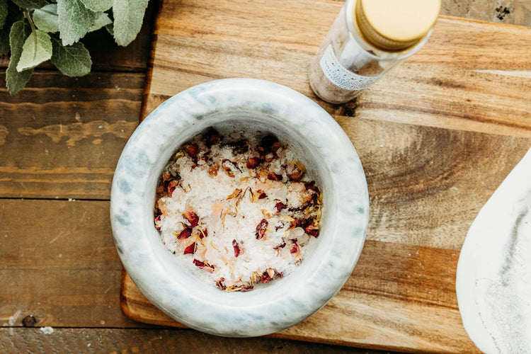 Bath salts in marble bowl on top of a wooden cutting board.