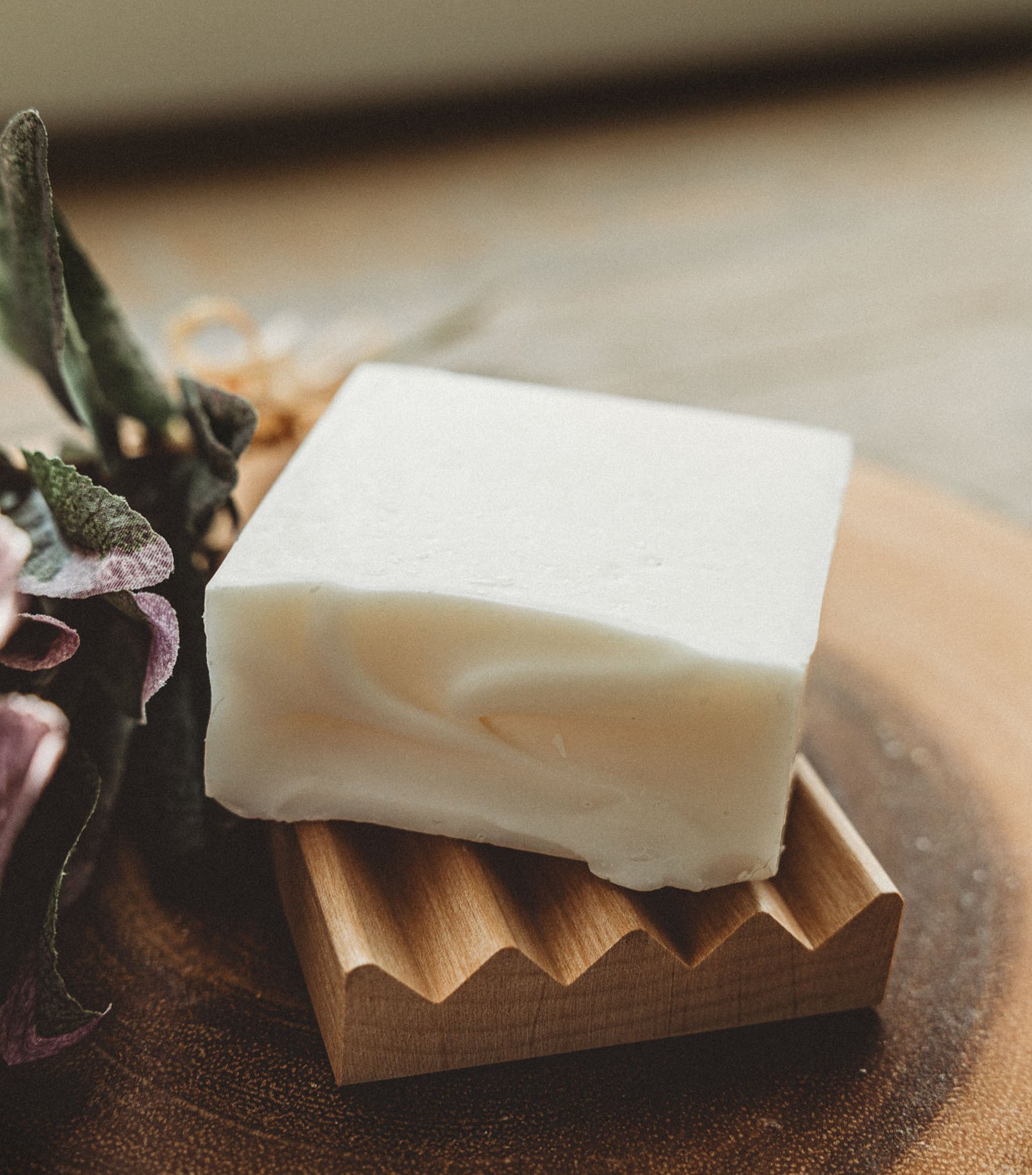 Bar of white soap on a wooden soap dish with a natural background