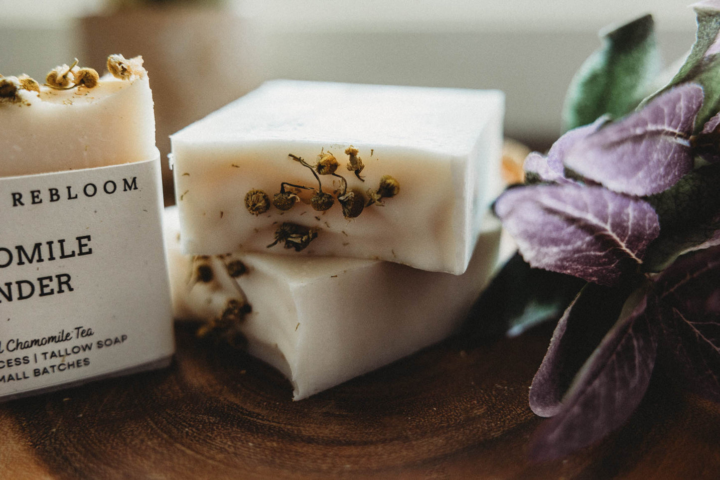 Three bars of chamomile lavender soap with Bohemian Rebloom label on a wooden board with dried lavender flowers.