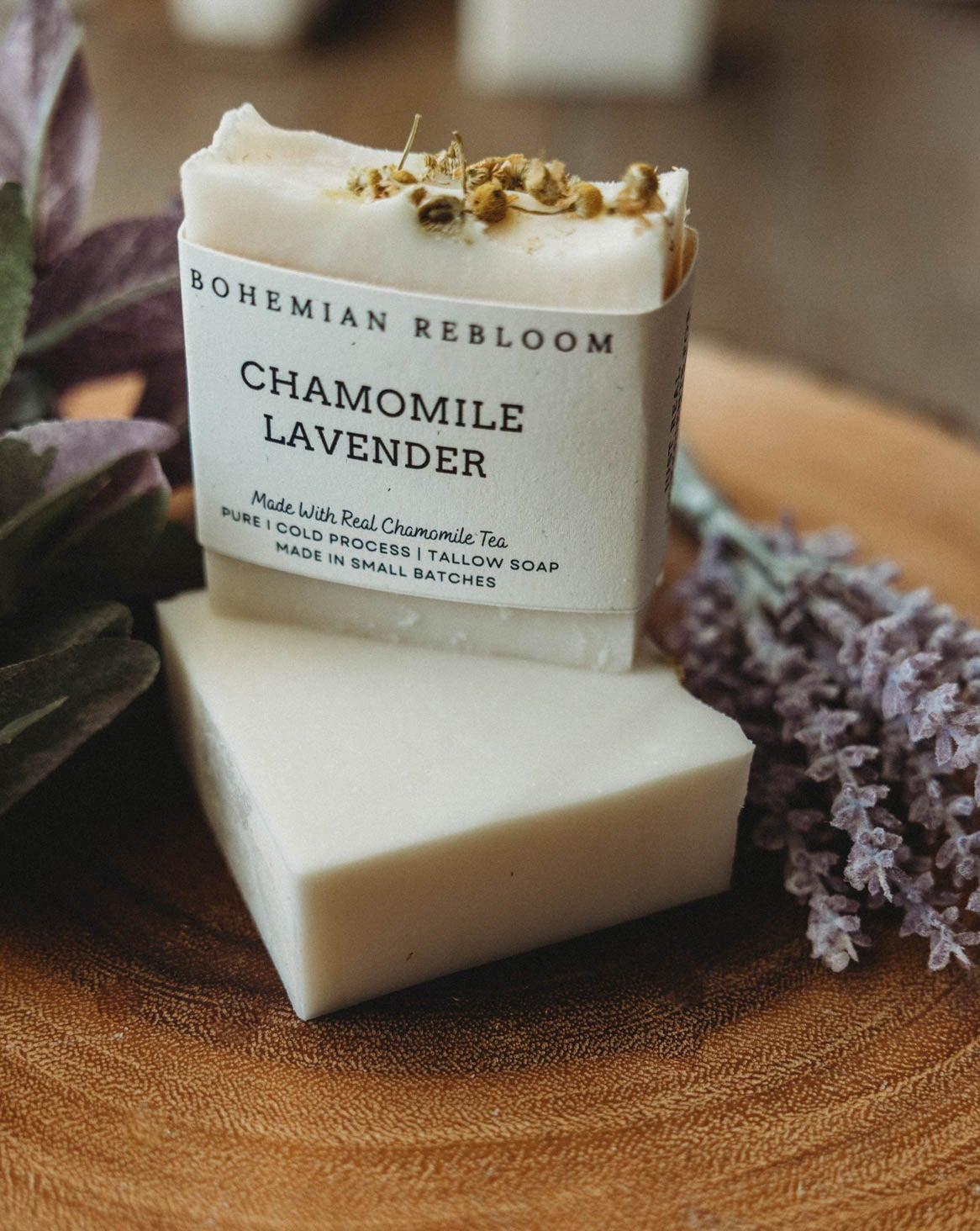 Two bars of chamomile lavender soap with Bohemian Rebloom label on a wooden board with dried lavender flowers.