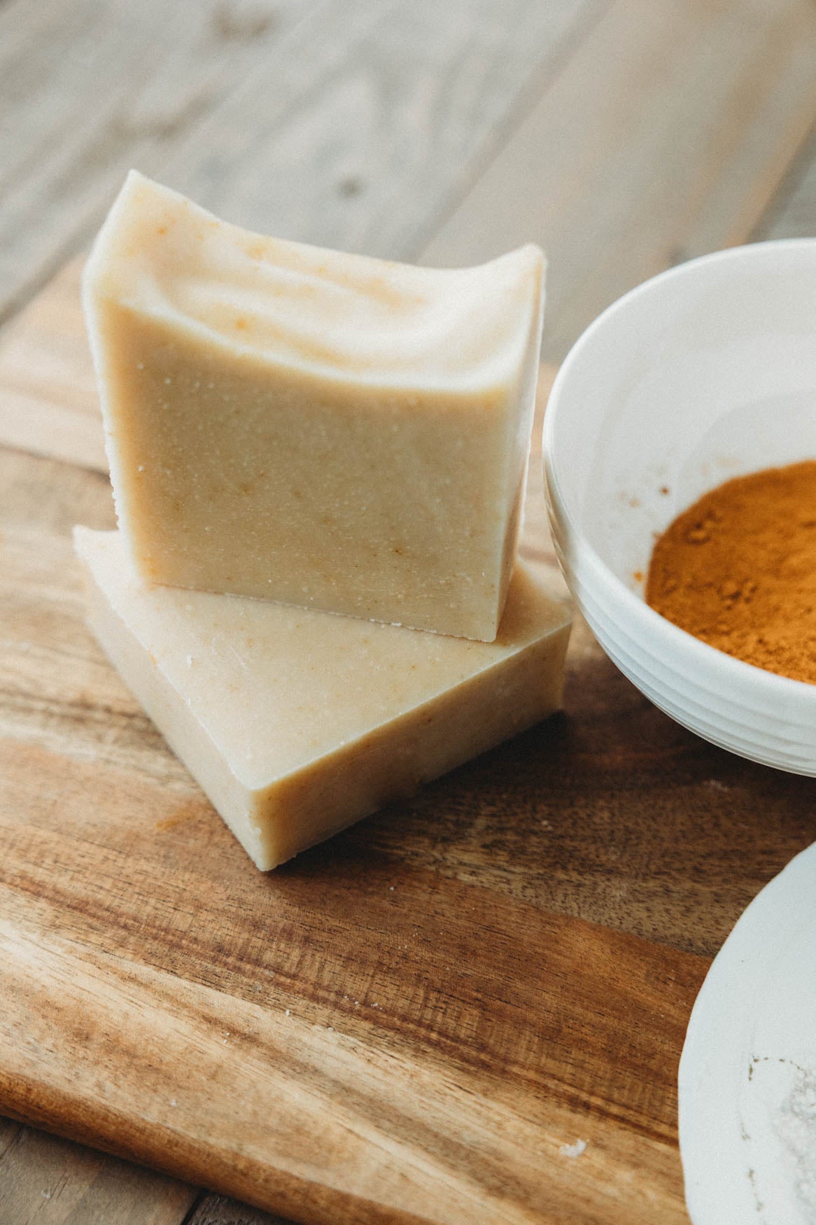 Two bars of honey chai turmeric soap with a bowl of turmeric powder on a wooden surface