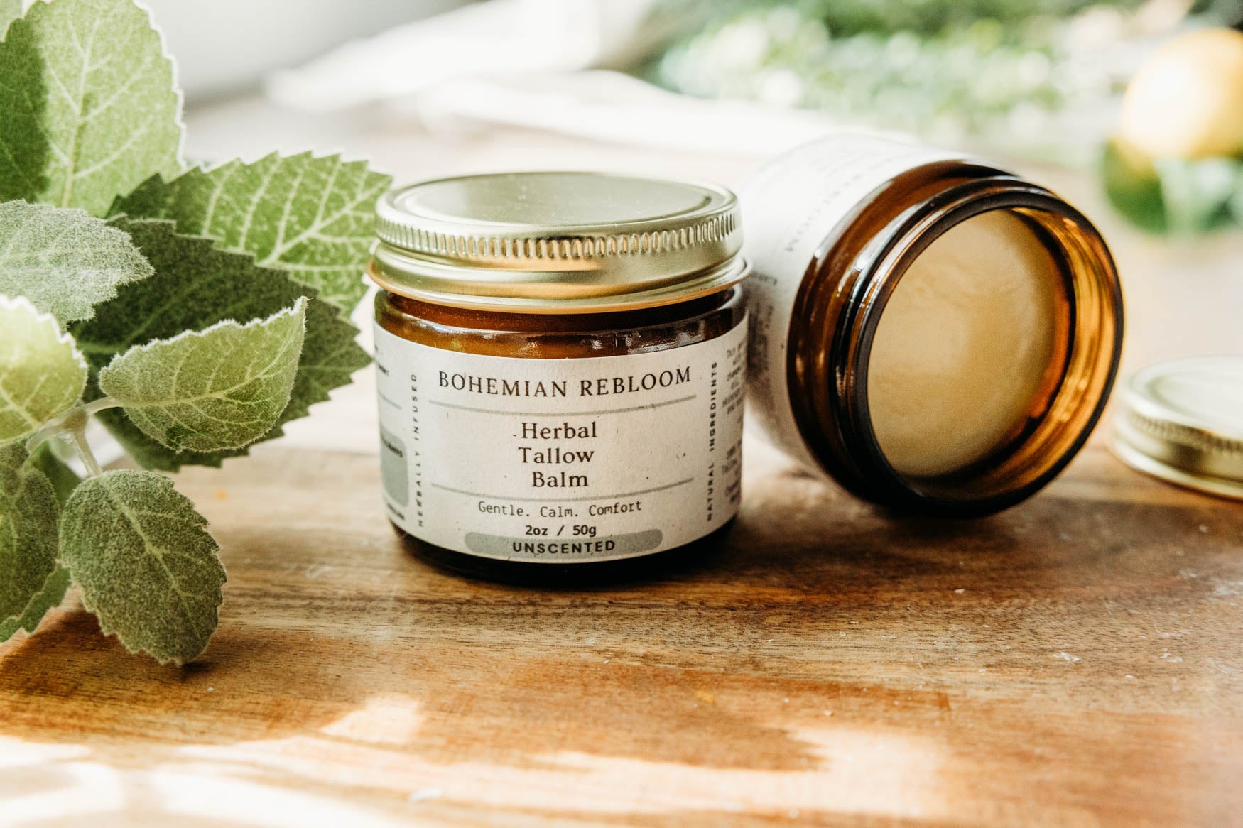 Jar of Bohemian Rebloom Herbal Tallow Balm on a wooden cutting board with green leaves in the background.