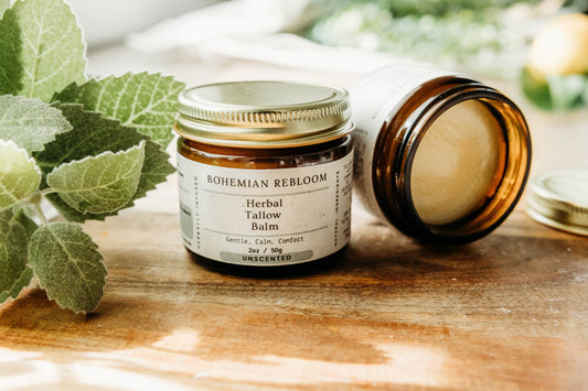 Jar of Bohemian Rebloom Herbal Tallow Balm on a wooden cutting board with green leaves in the background.