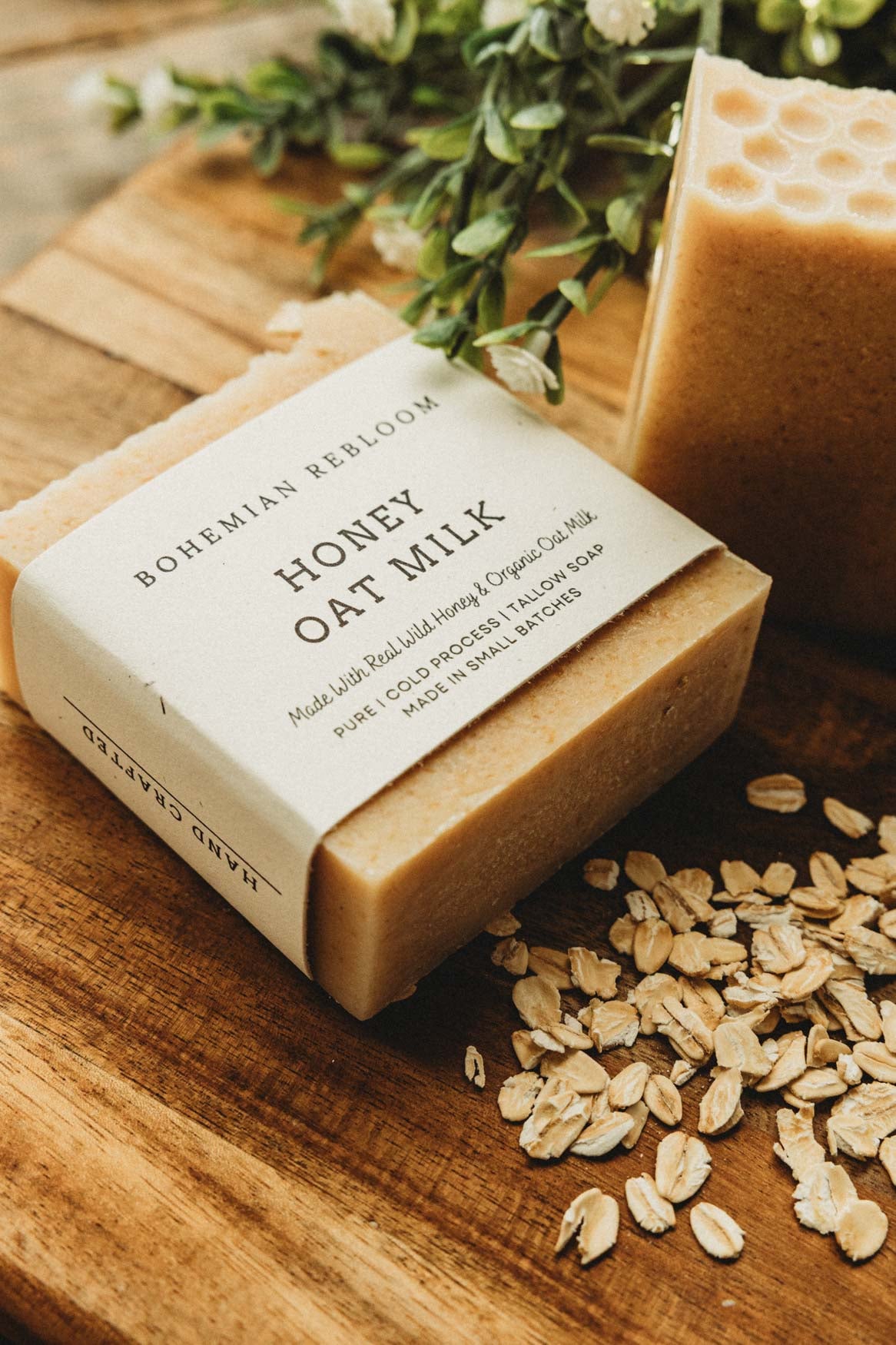 Bar of honey oat milk soap with a label on a wooden surface with oats and greenery.