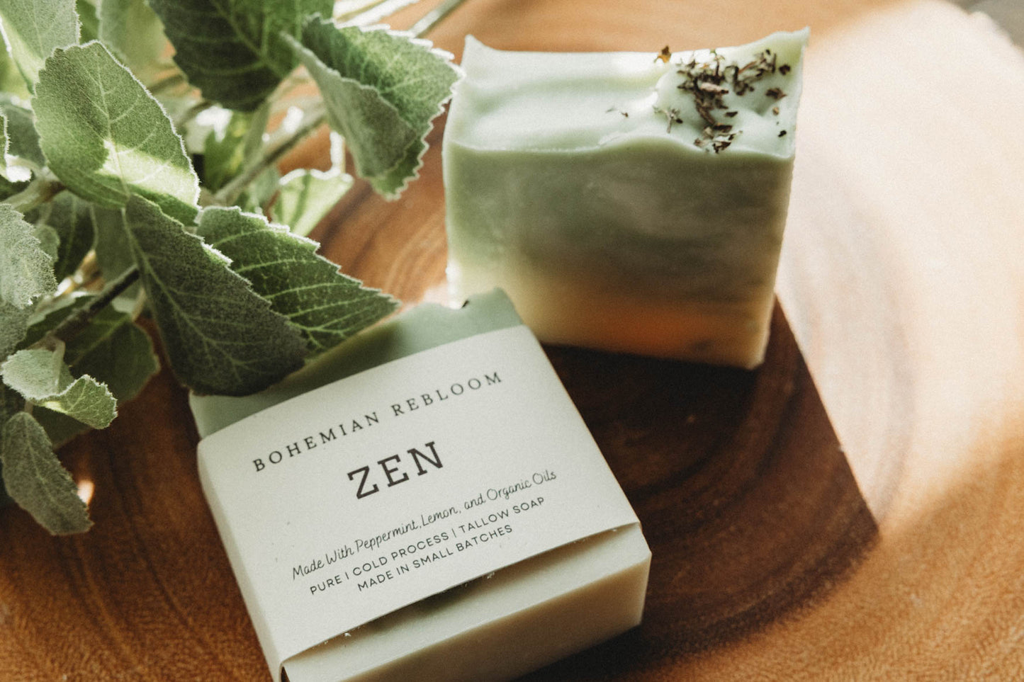 Bar of green and white swirled soap with packaging labeled 'Zen' on a wooden surface with greenery.