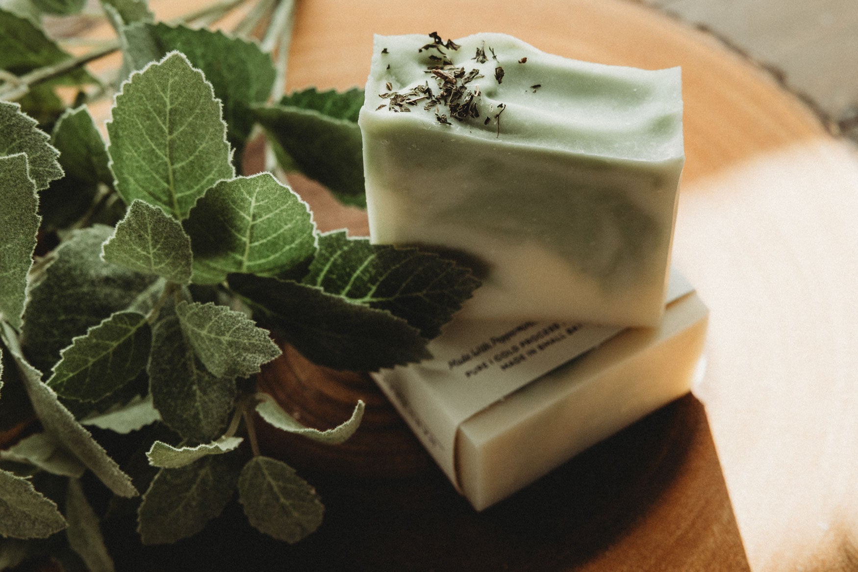 Two bars of green and white swirled soap with packaging labeled 'Zen' on a wooden surface with greenery.