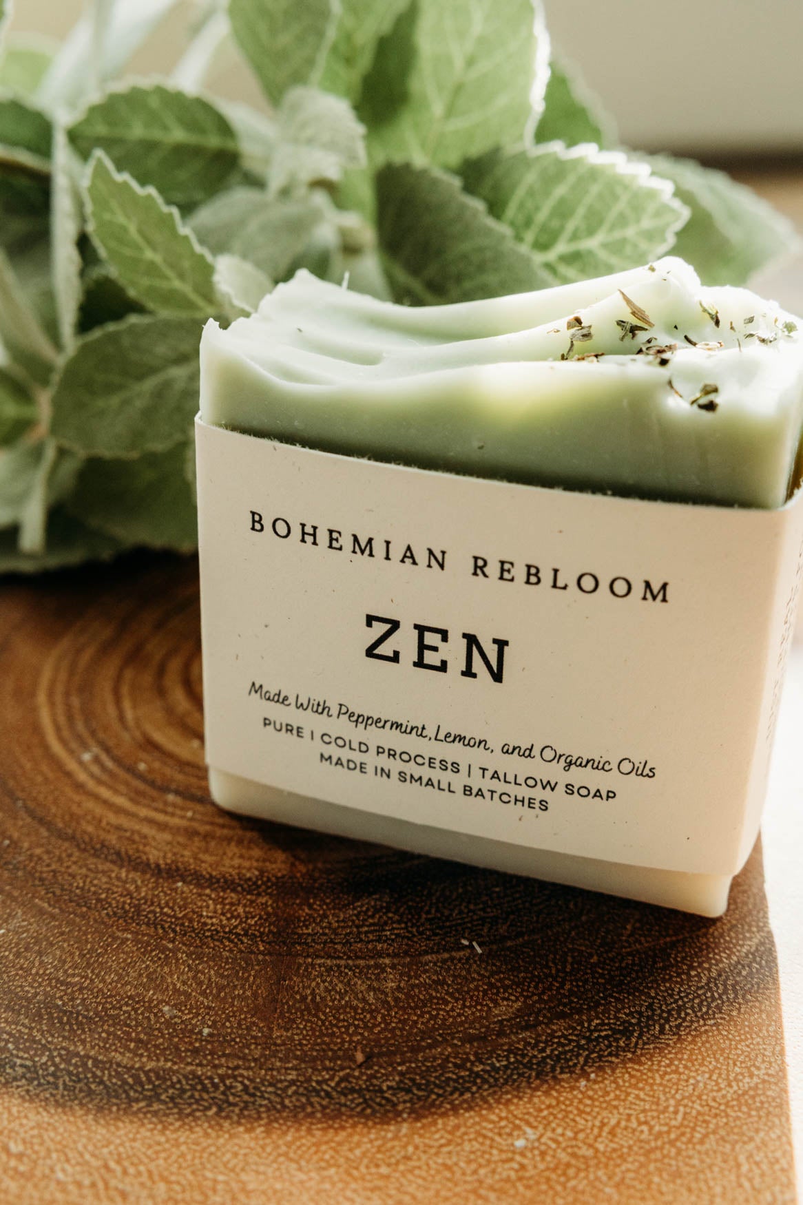 Green bar of cold process soap with 'Bohemian Rebloom Zen' label on a wooden surface with green leaves.