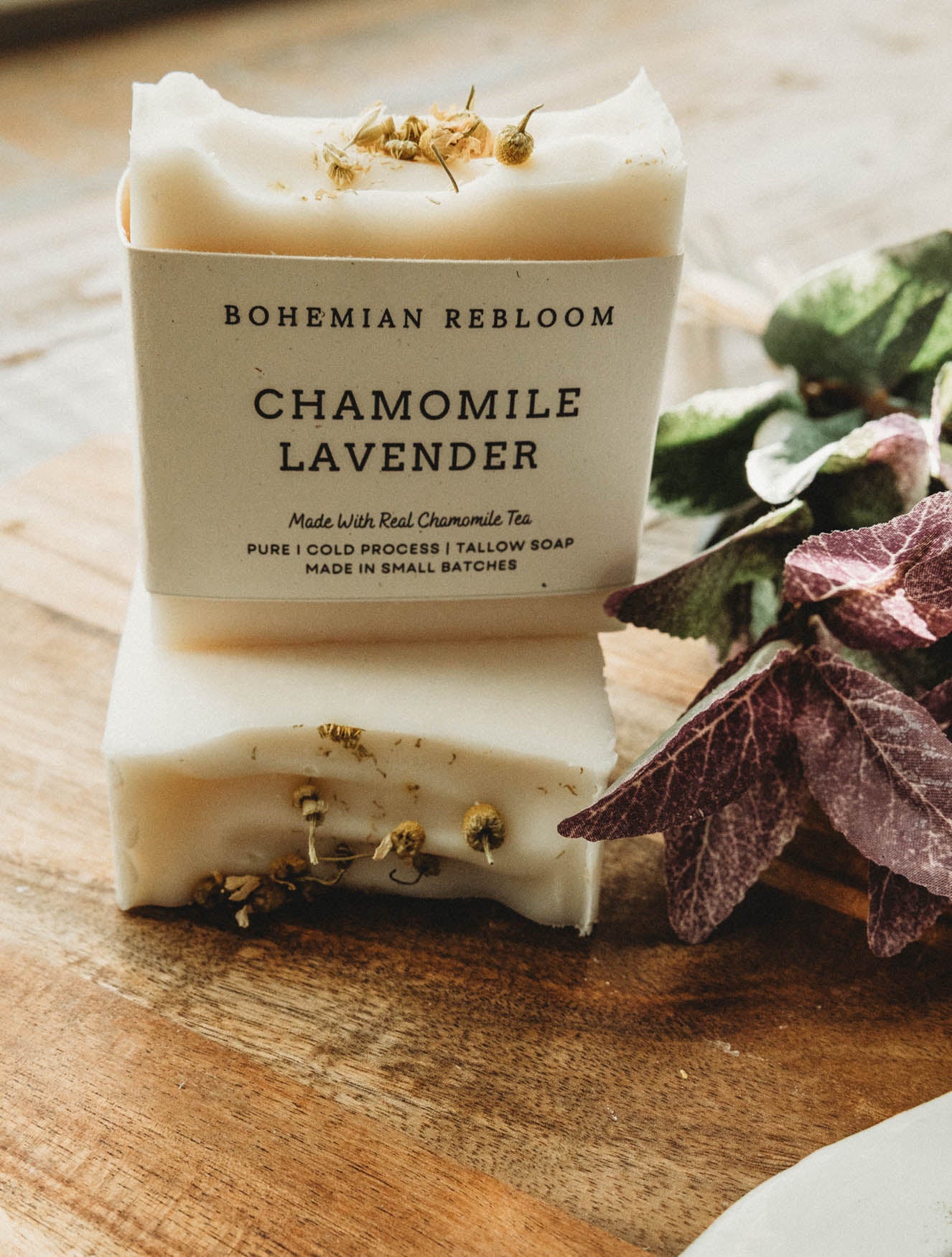 Two bars of chamomile lavender soap with Bohemian Rebloom label on a wooden board with dried lavender flowers.