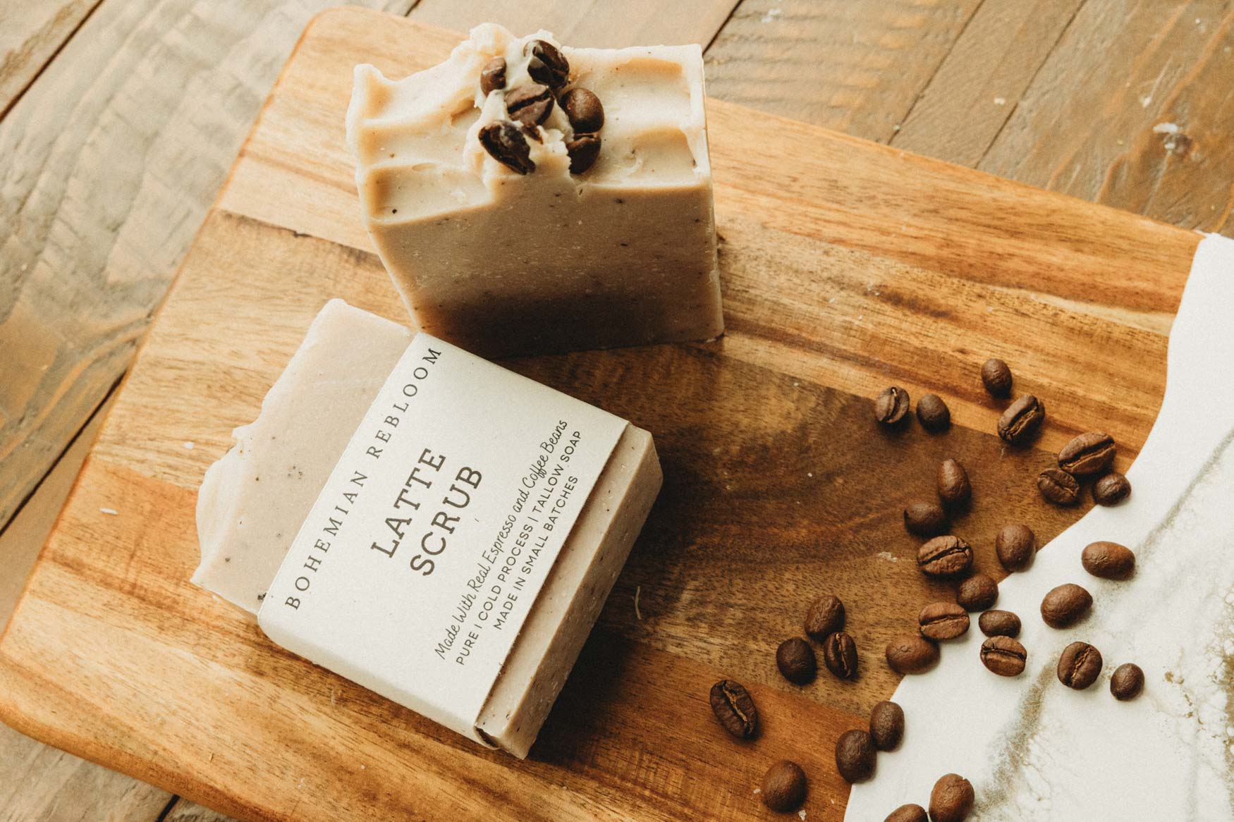 Two bars of coffee-scented soap on a wooden cutting board with scattered coffee beans.
