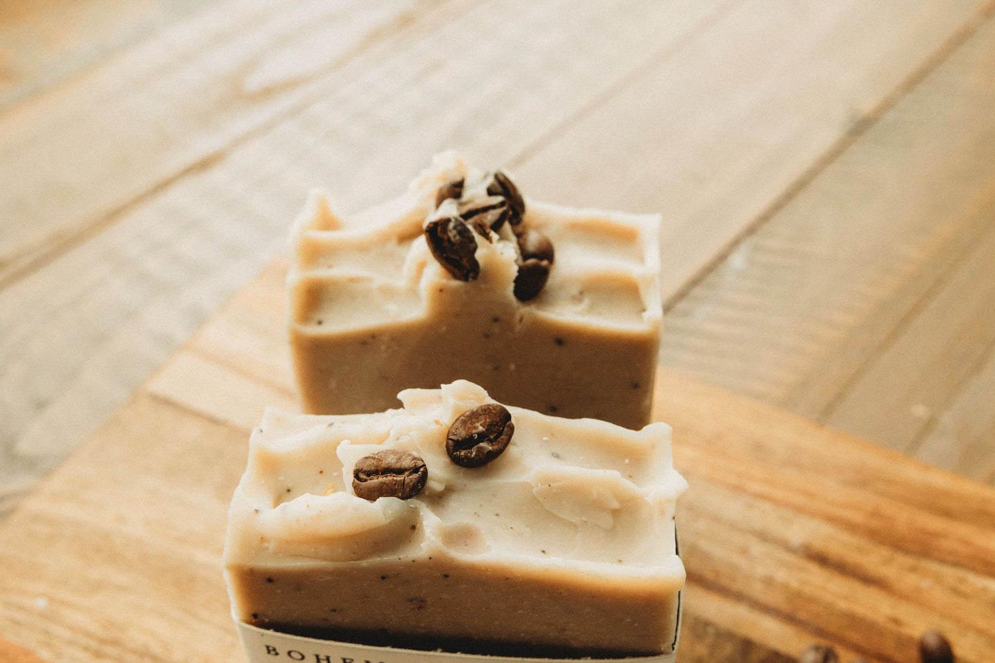 Two bars of soap with coffee beans on a wooden surface