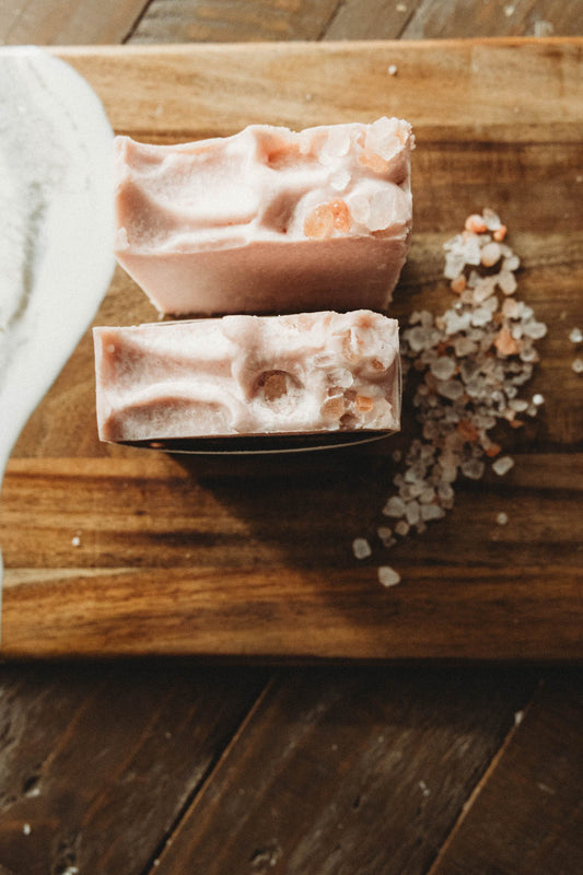Two soap bars on a wooden cutting board with sea salt crystals.
