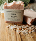 Bar of pink salt soap with packaging on a wooden surface