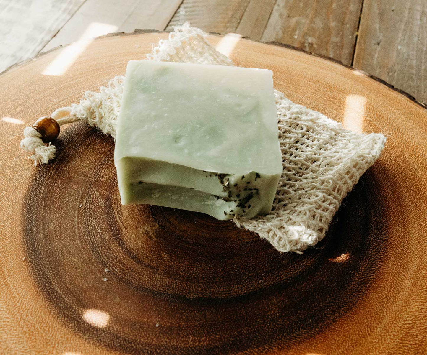 Green soap bar with black specks on sisal soap saver bag on a wooden surface