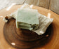 Green soap bar with black specks on sisal soap saver bag on a wooden surface