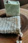 Soap saver bag with bar of green Zen soap in the background on top of a wooden board.