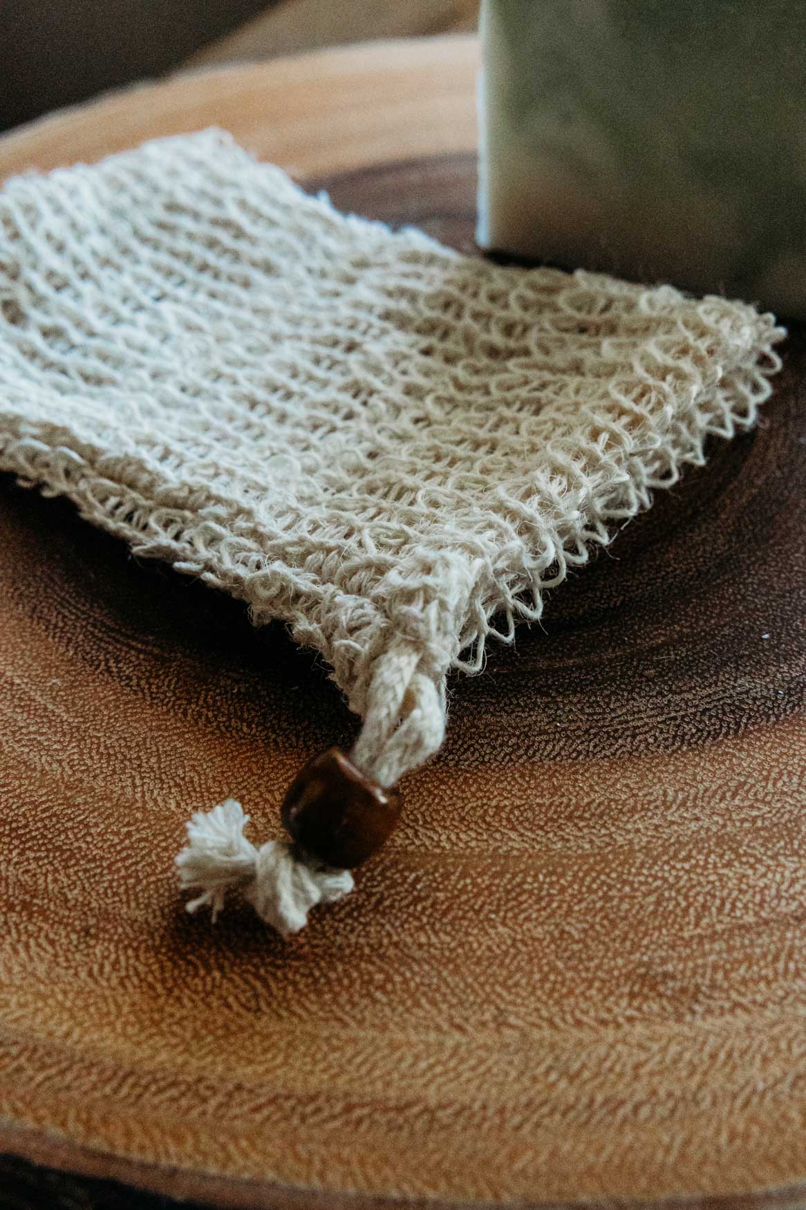 Soap saver bag with bar of soap in the background on top of a wooden board.