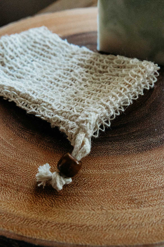 Soap saver bag with bar of soap in the background on top of a wooden board.