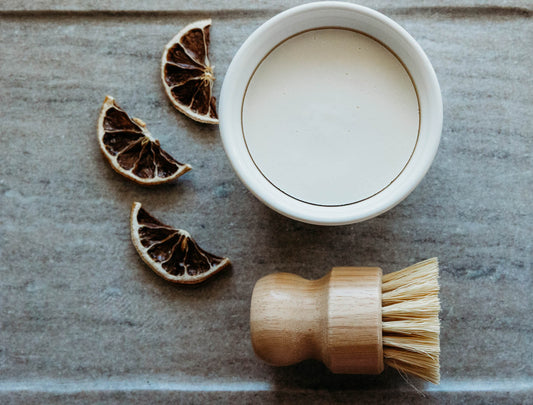 Ramekin dish filled with organic coconut and castor oil dish soap with brush laying on the side.