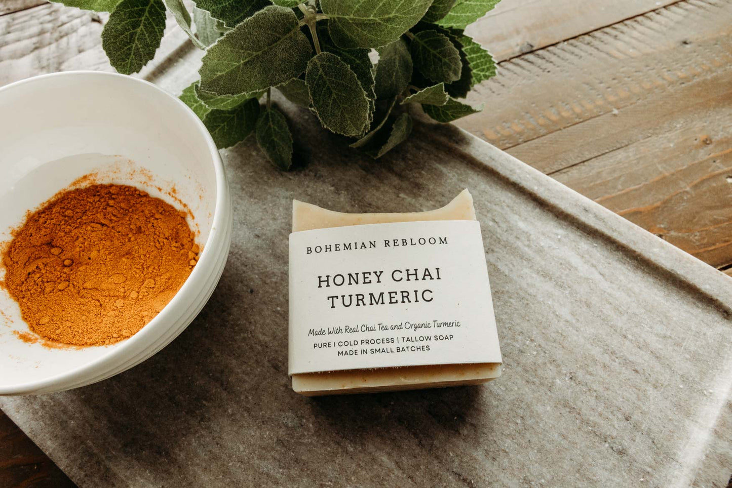 Bohemian Reblom Honey Chai Turmeric soap bar next to a bowl of turmeric powder on a wooden surface.