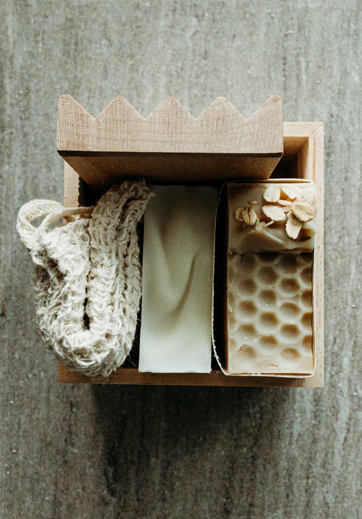 Wooden box with natural soap and scrubber on a natural surface.