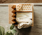 A bar of sweet almond and honey oat milk soap with a soap saver and  wooden soap dish on a marble table with greenery in the background.