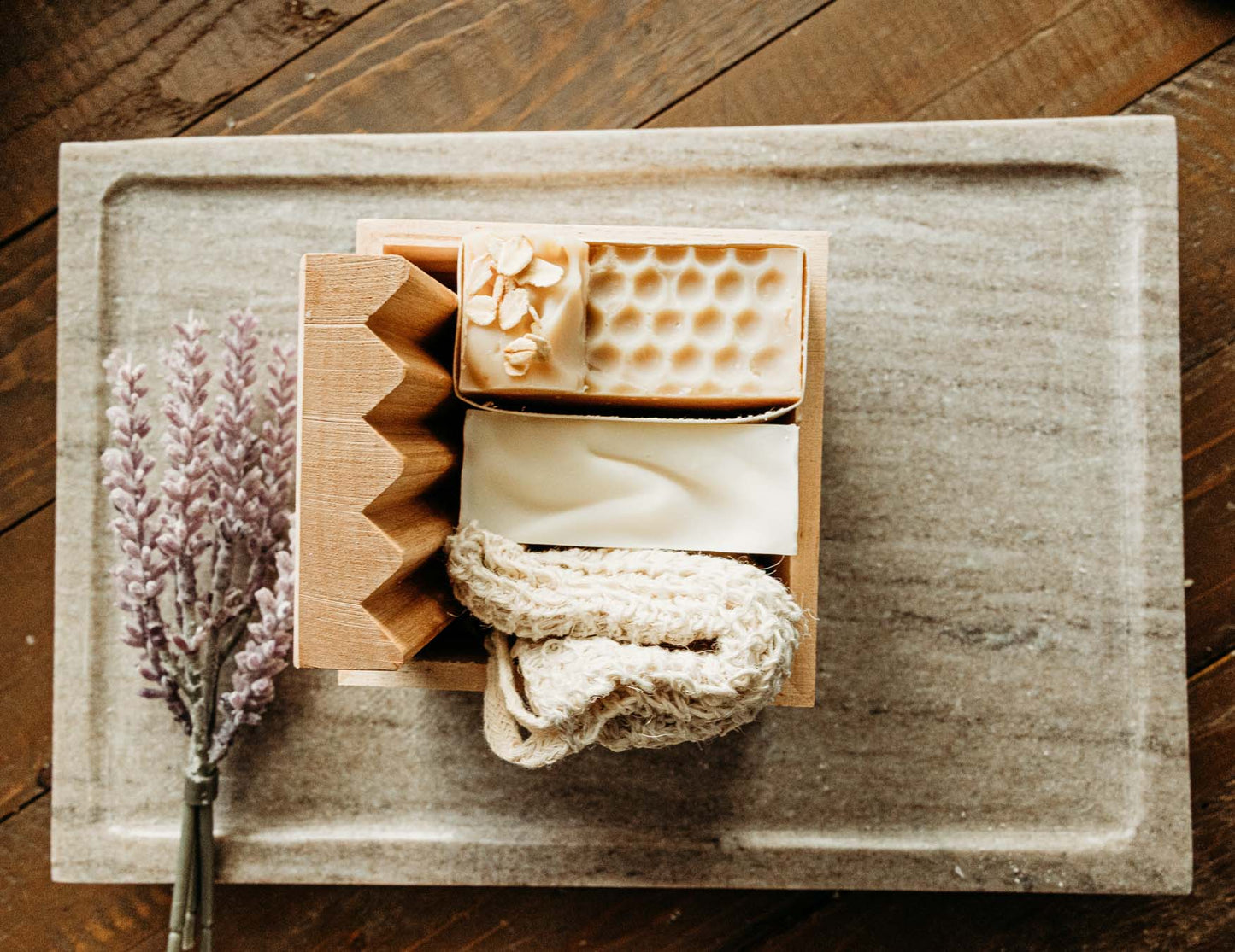 Two bars of soap in a wooden box on a wooden surface with a lavender flower.