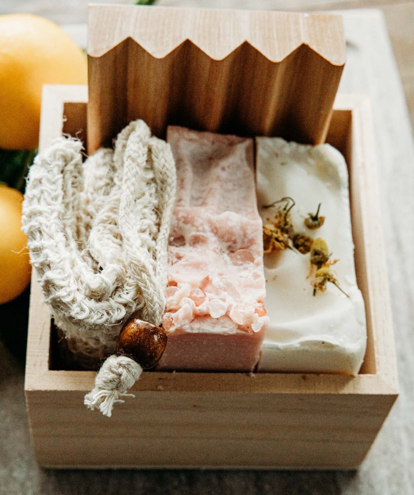 A close up of a bar of himalayan sea salt soap, lavender chamomile soap, a soap saver, and wooden soap dish onto of a marble board.