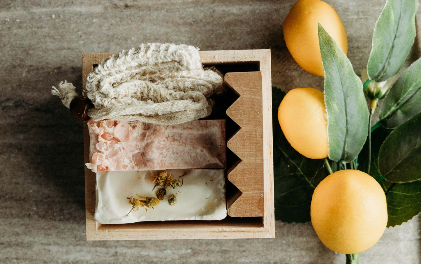 Two bards of soap in a wooden box with lemons and leaves on a wooden surface