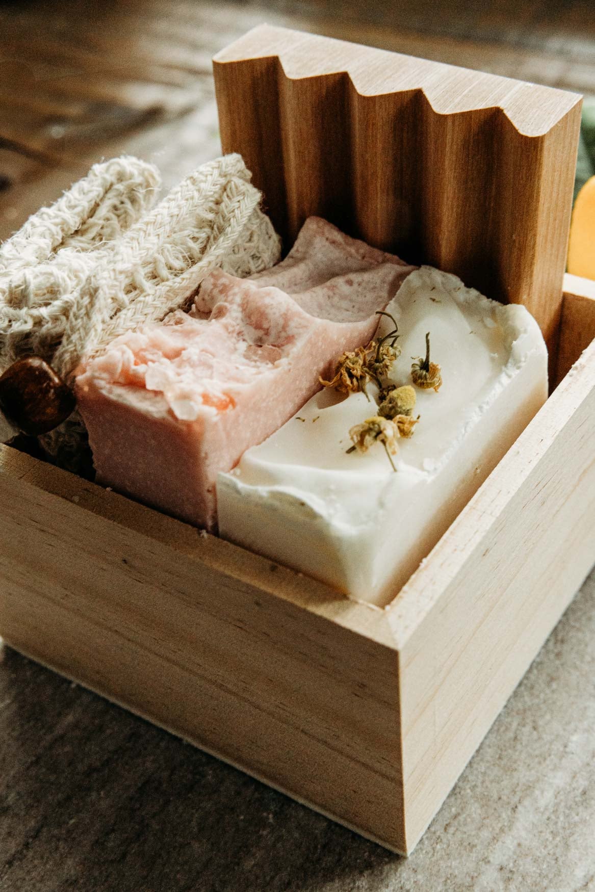 A bar of himalayan sea salt soap, lavender chamomile soap, a soap saver, and wooden soap dish onto of a marble board.