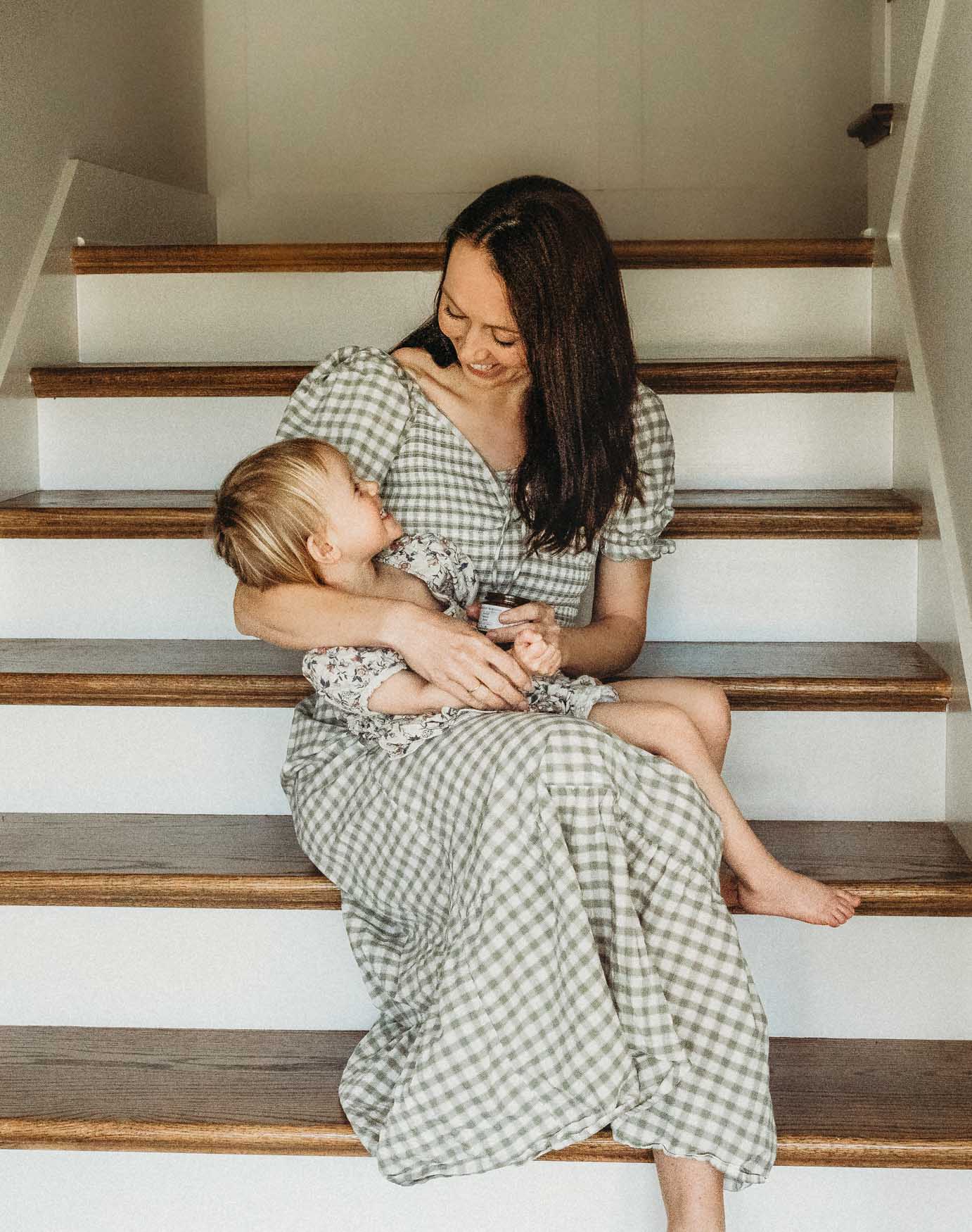 Woman and child sitting on a staircase wearing matching green checkered dresses.