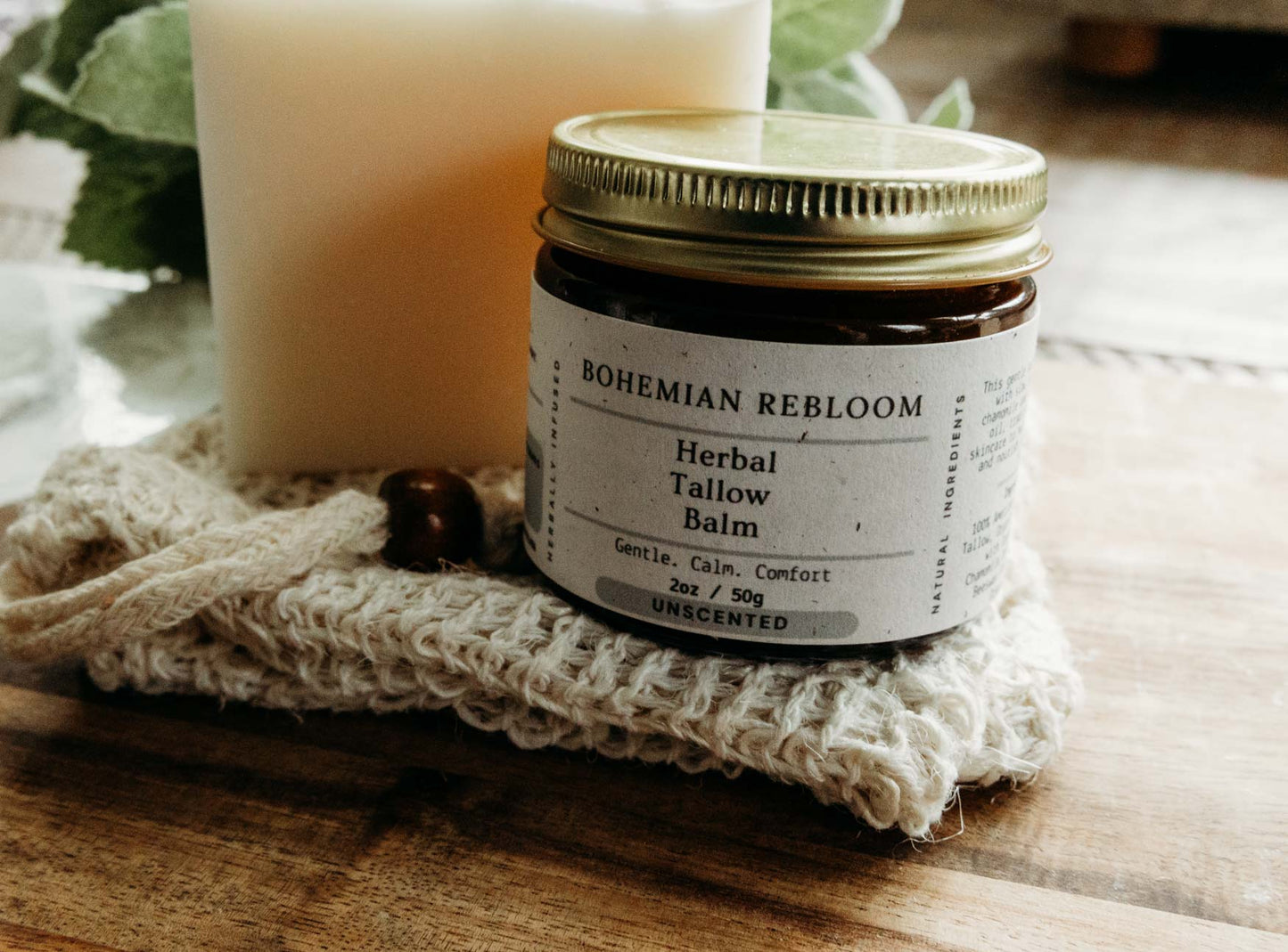 Jar of Bohemian Rebloom Herbal Tallow Balm on a textured surface with a bar of Sweet Almond in the back sitting on top of a soap saver bag.