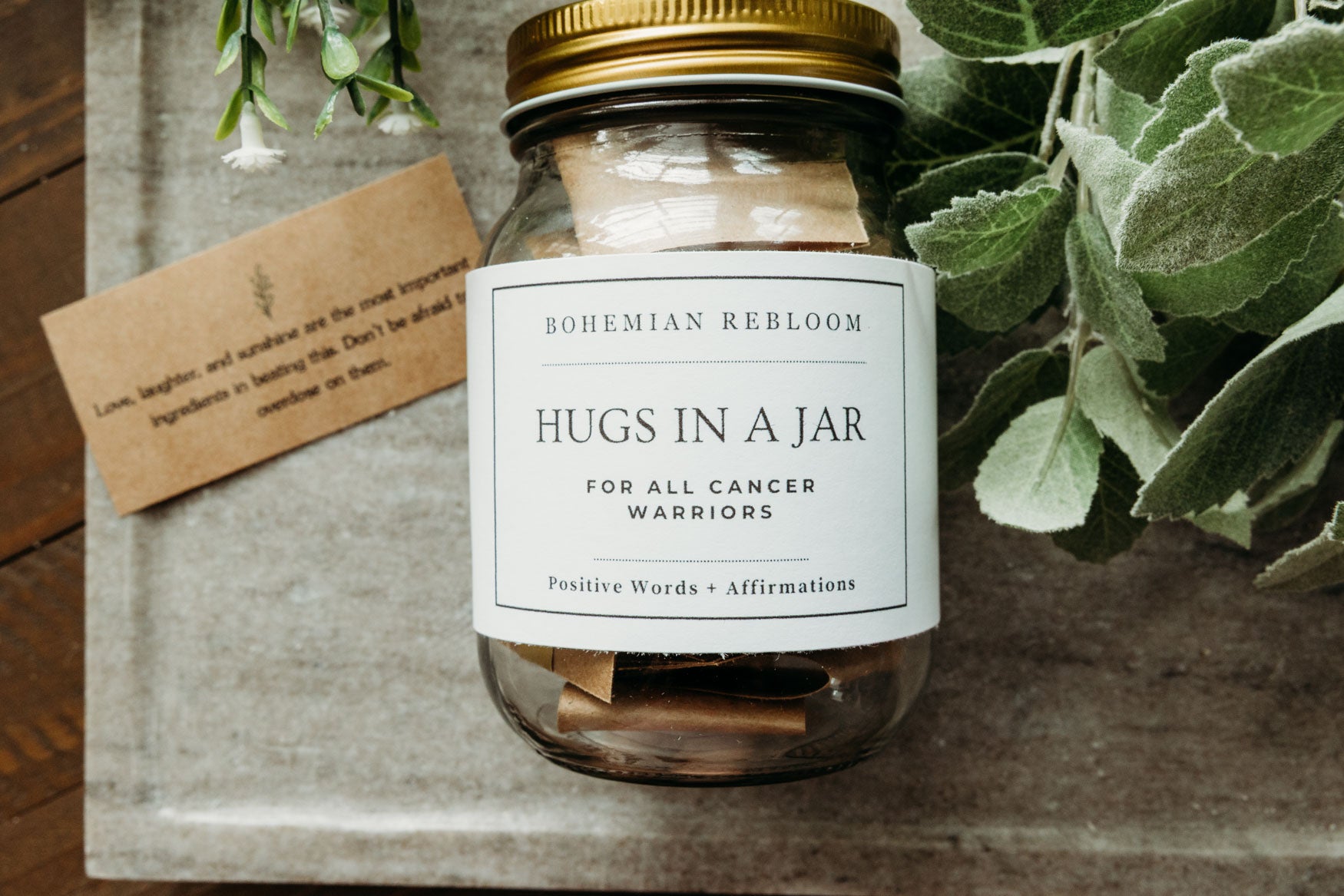 Jar labeled 'Hugs in a Jar' with a tag on a wooden surface with greenery.