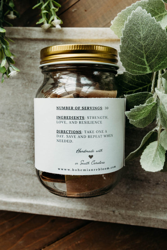 Jar with a gold lid and white label on a wooden surface with greenery