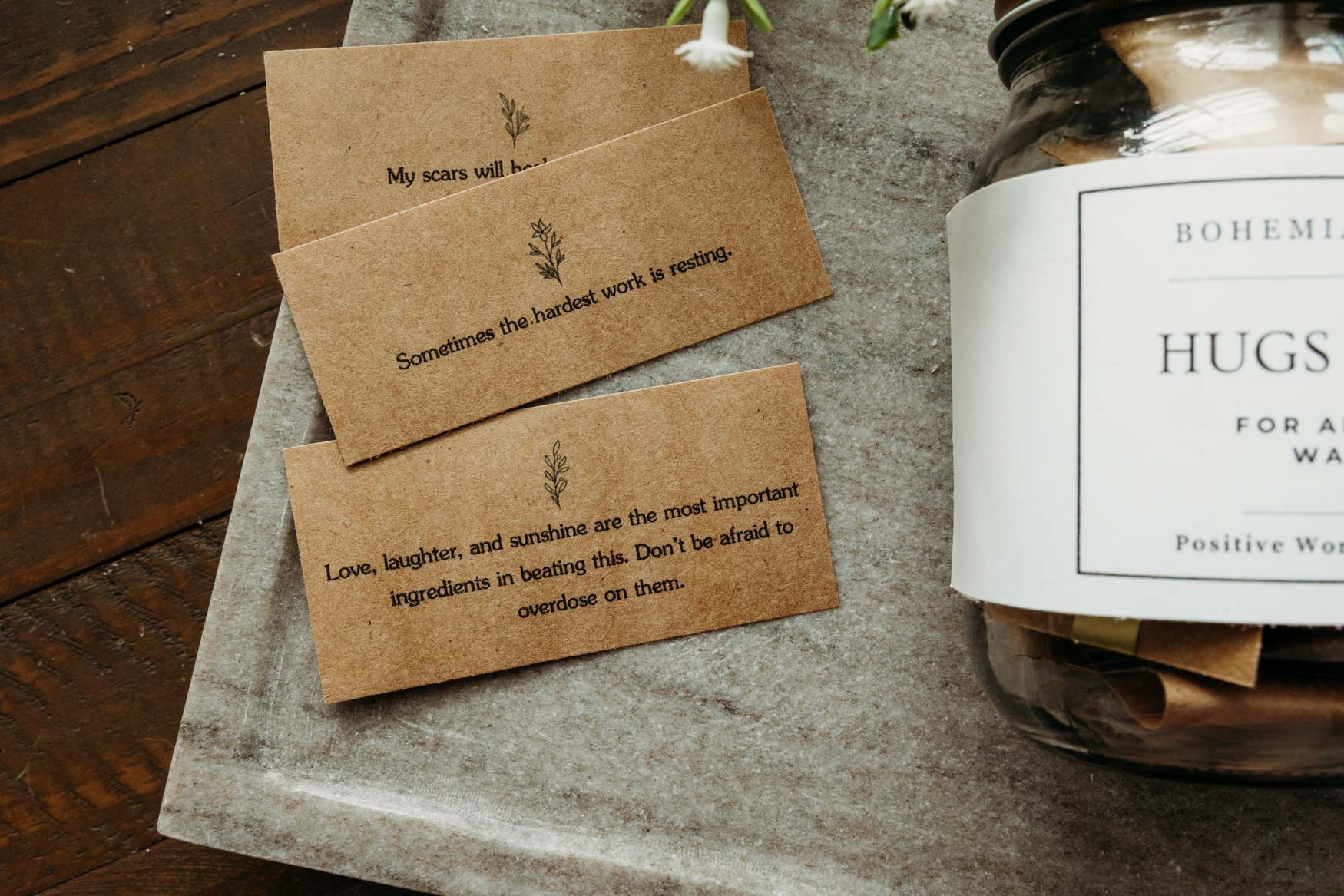 Two motivational cards on a wooden surface with a jar labeled 'Hugs' in the background.