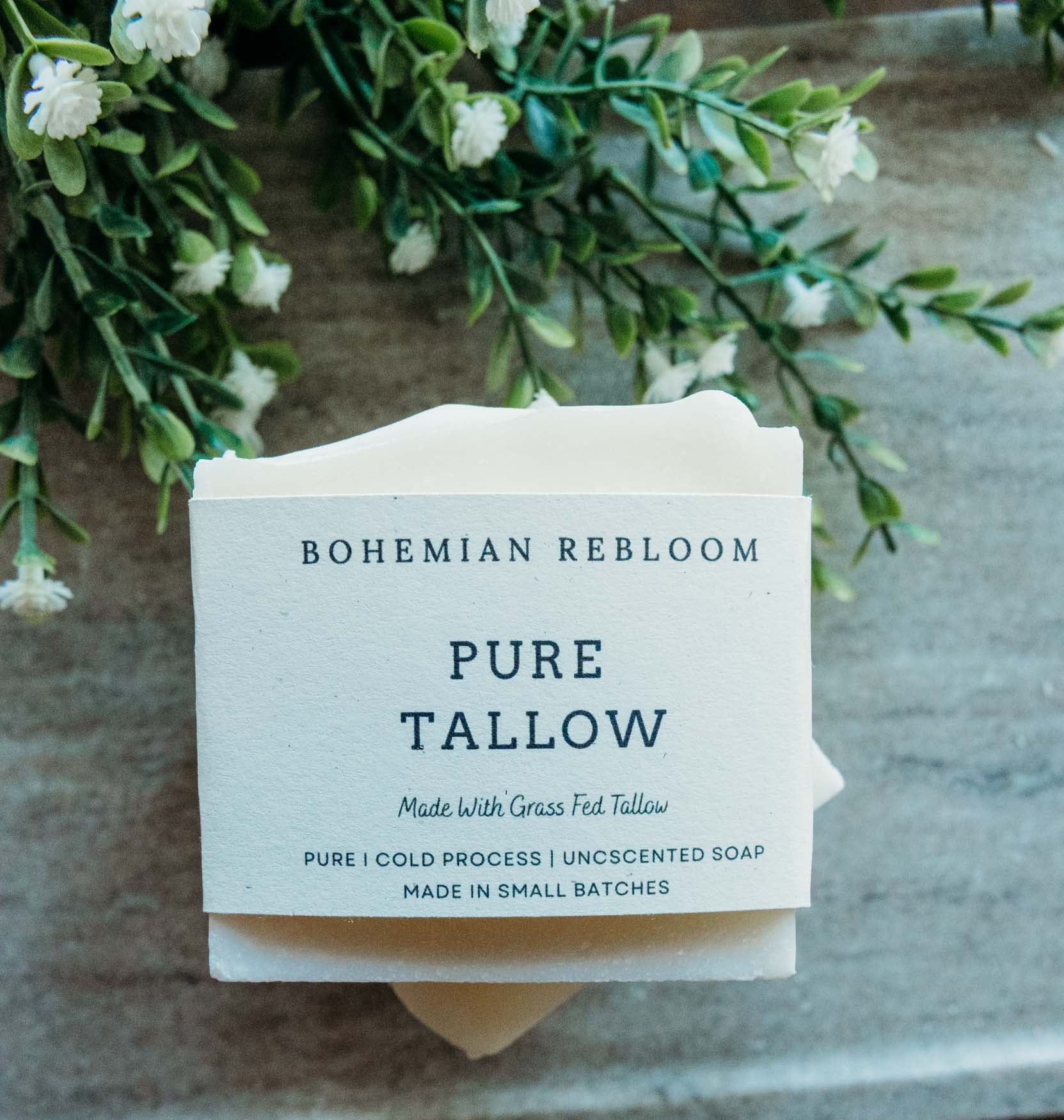 Bar of soap with 'Bohemian Rebloom' Pure Tallow Soap label on a stone surface with greenery.