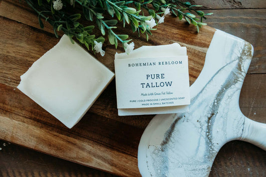 Two bars of pure grass fed tallow soap  on a wooden surface with greenery