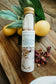 Bottle of 'Refresh' bath salt with lemons and rose petals on a wooden surface