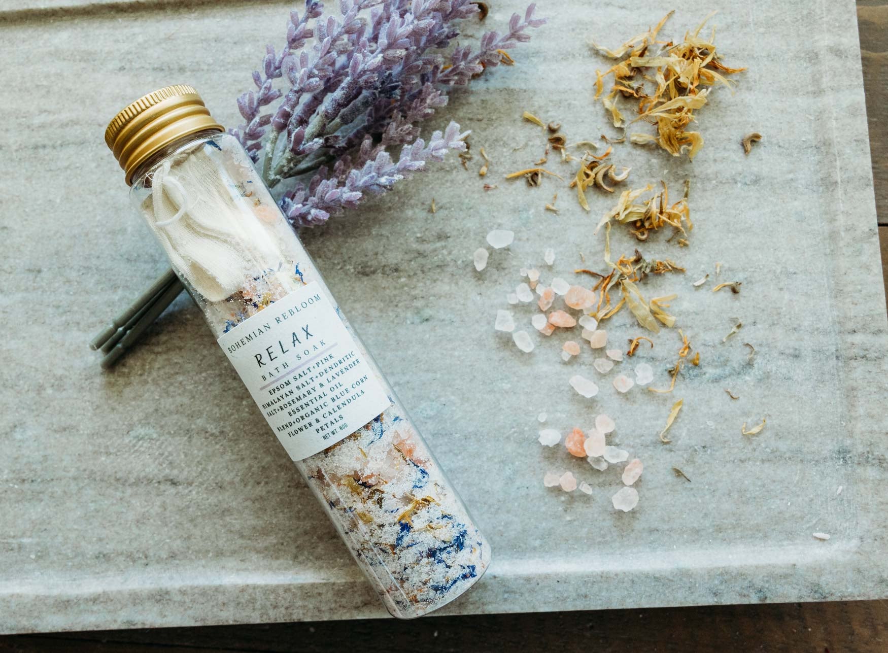 Bottle of Relax bath salts with lavender and flowers on a stone surface