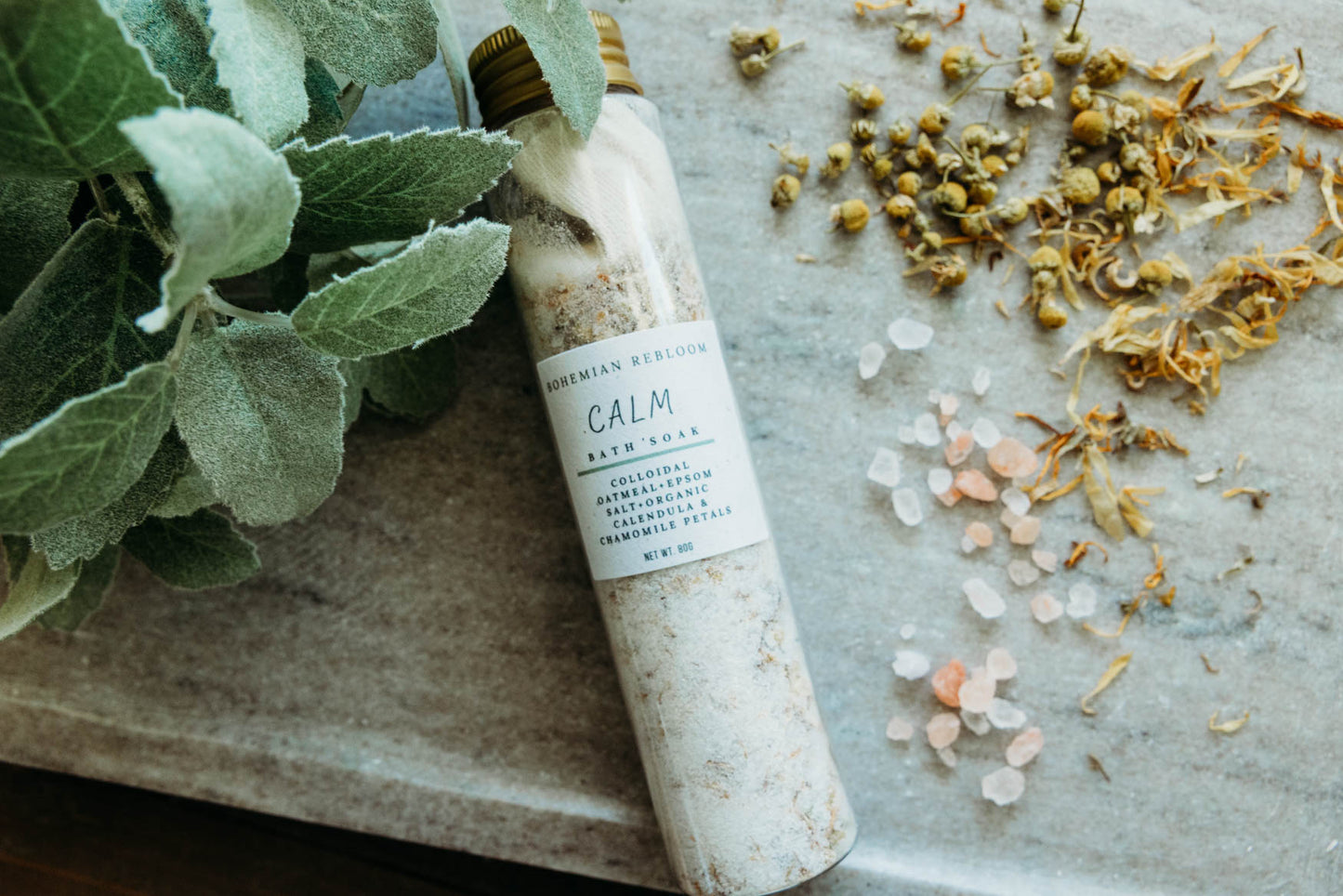 Bottle labeled 'Calm' with bath salts  and herbs on a stone surface