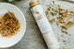 Bath salt tube labeled 'Calm' next to a bowl of dried herbs on a textured surface