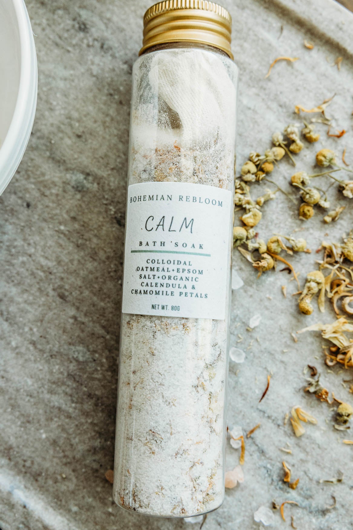 Bath soak bottle labeled 'Calm' on a stone surface with dried flowers.