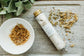 Bottle of bath salts labeled 'Calm' on a stone surface with dried herbs and a leafy plant.
