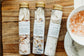 Three test tube bottles of bath salts laying flat on a wooden cutting board with a bowl of salts nearby.