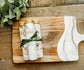 Three bottles of bath salts wrapped  with a green bow on a wooden cutting board.
