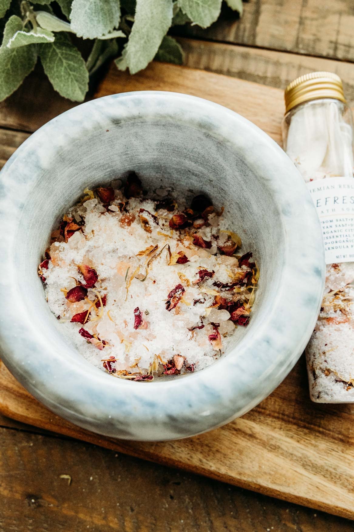 Marble bowl with bath salts and a bottle of bath salts on a wooden surface