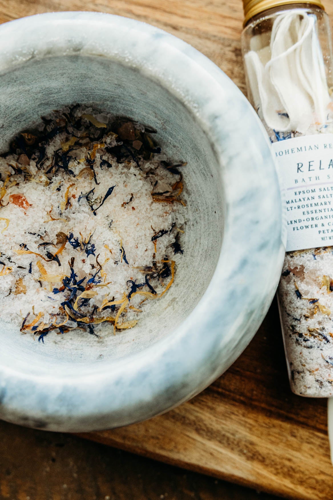 Mortar and pestle with bath salts and a bottle of bath salts on a wooden surface