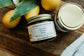 Jar of Bohemian ReBloom Creamy Tallow Balm on a wooden surface with fruits and leaves.