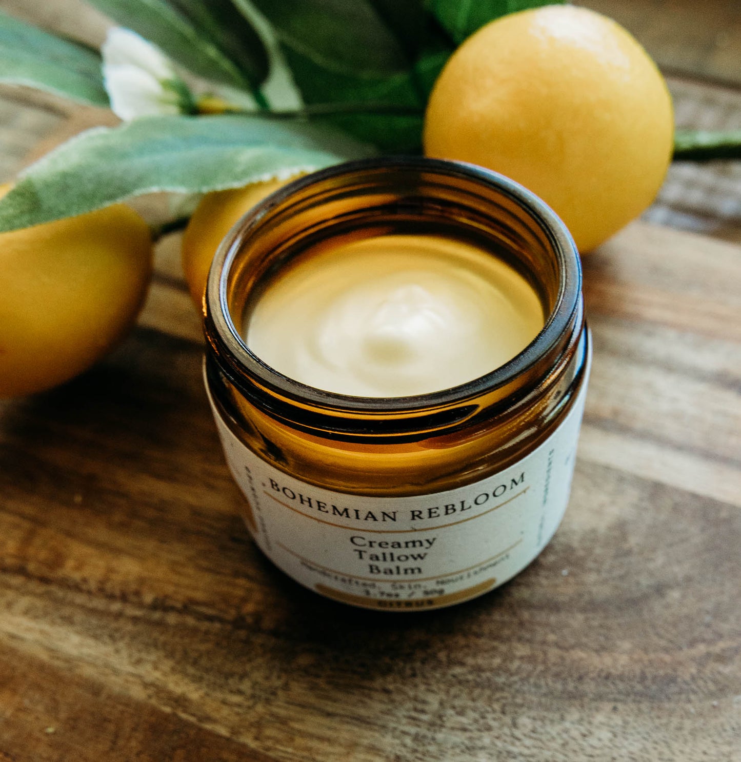 Jar of creamy tallow balm with lemons and leaves on a wooden surface